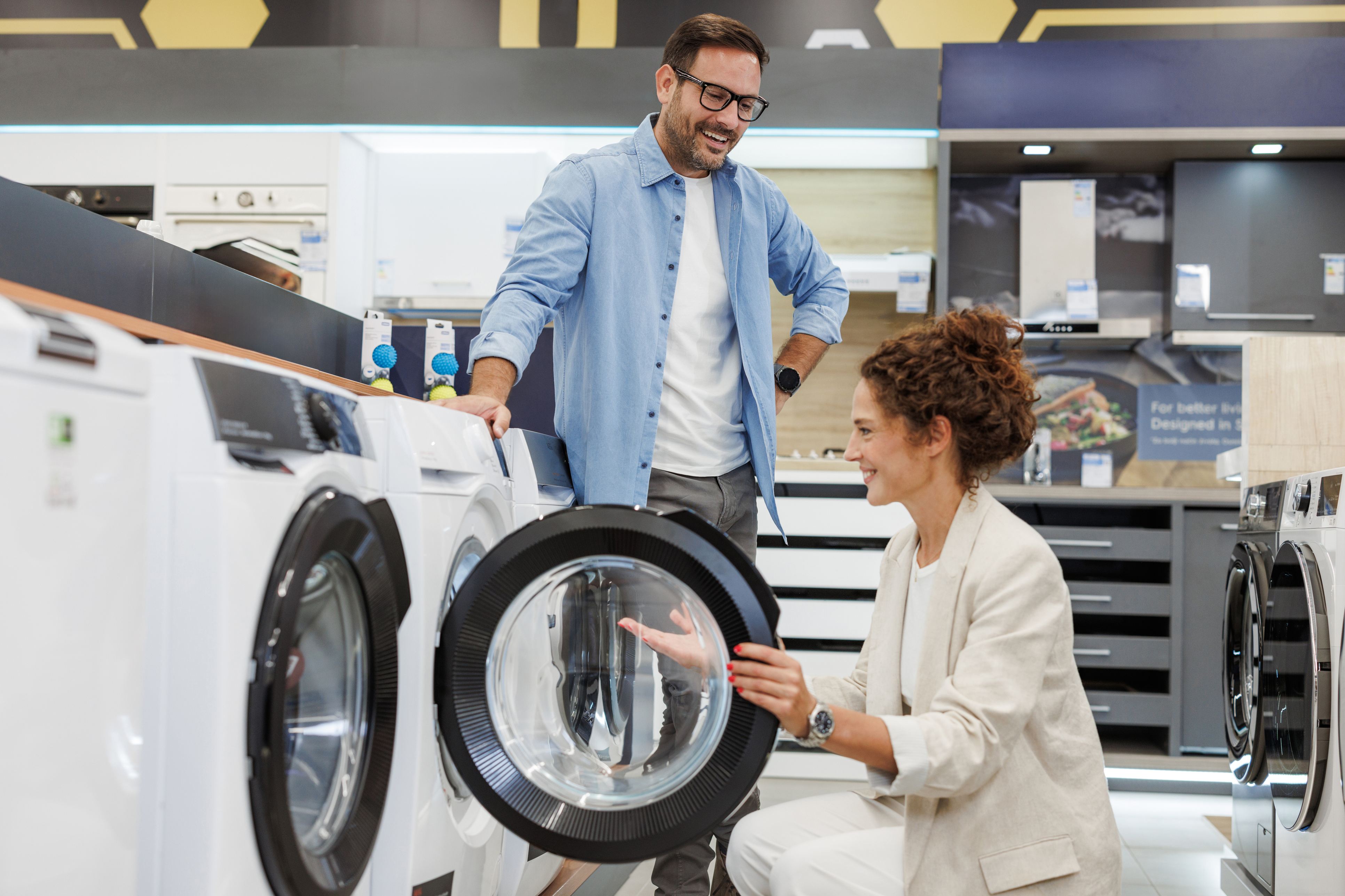 A smiling, standing man and crouching woman inspecting a washer in a store